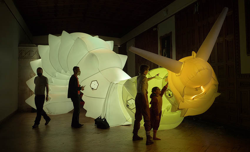 4 people stand infront of a large inflatable soft robotic creature